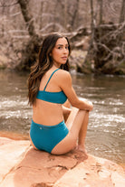 Woman outdoors in two-piece swimsuit featuring mid-rise, cheeky bottoms ready for adventure.