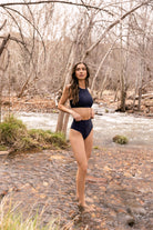 Women outdoors in navy blue two-piece swimsuit with full coverage, trapeze style top featuring a strappy razorback design enjoying nature. 