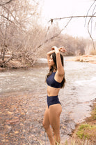 Women outdoors in navy blue two-piece swimsuit with high waist, cheeky bottoms enjoying nature.